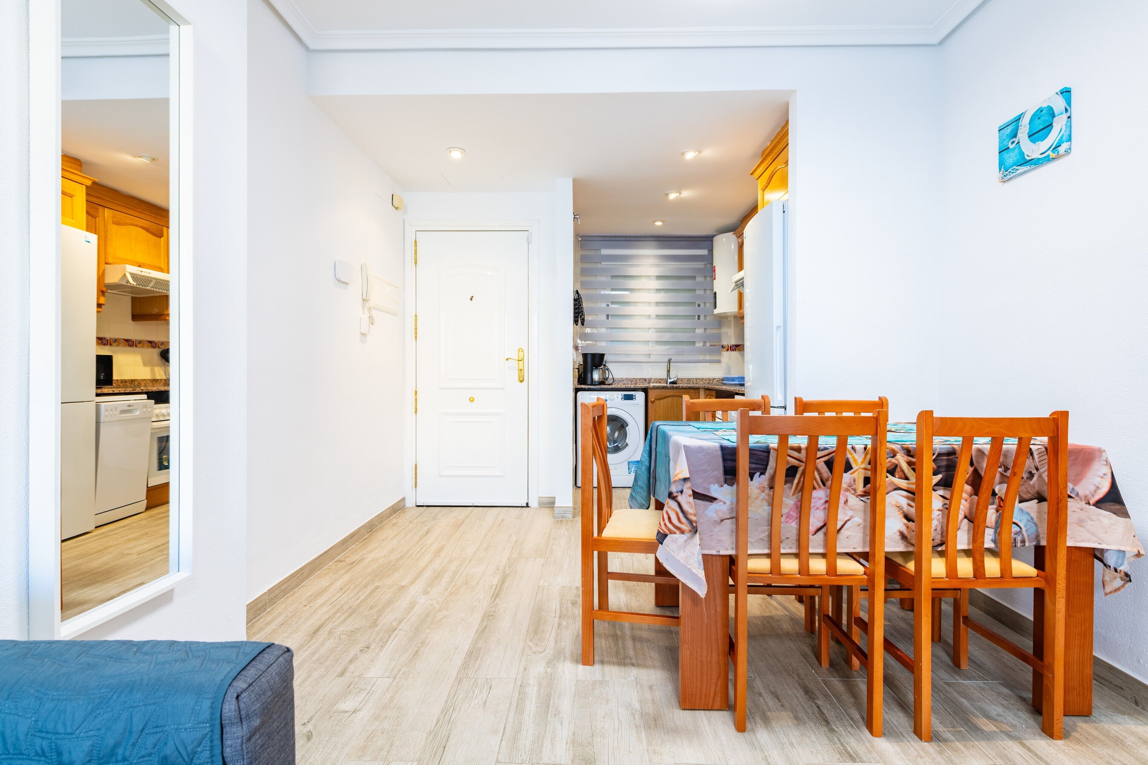 A dining area with a table and chairs, a kitchen in the background, and a door leading to another room.