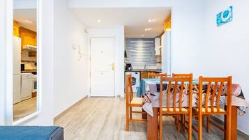 A dining area with a table and chairs, a kitchen in the background, and a door leading to another room.
