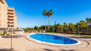 Une piscine à bord incurvé, entourée d’une zone pavée, avec un bâtiment visible en arrière-plan.