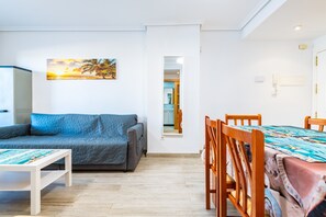 Olohuoneessa on sohva, ruokapöytä tuoleineen, seinällä taulu ja ovi, joka johtaa toiseen huoneeseen.