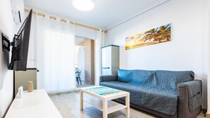Un salon comprenant un canapé, une table basse, un téléviseur à écran plat fixé au mur et une porte donnant sur une autre pièce.