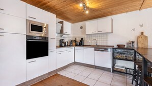 Una cocina moderna con armarios blancos, horno empotrado, microondas y cafetera.