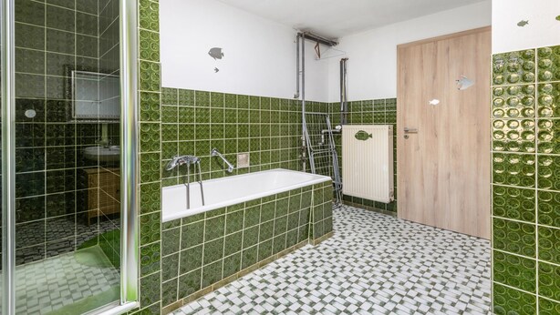 Un baño con baldosas verdes estampadas, una bañera blanca, una zona de ducha y una puerta de madera.