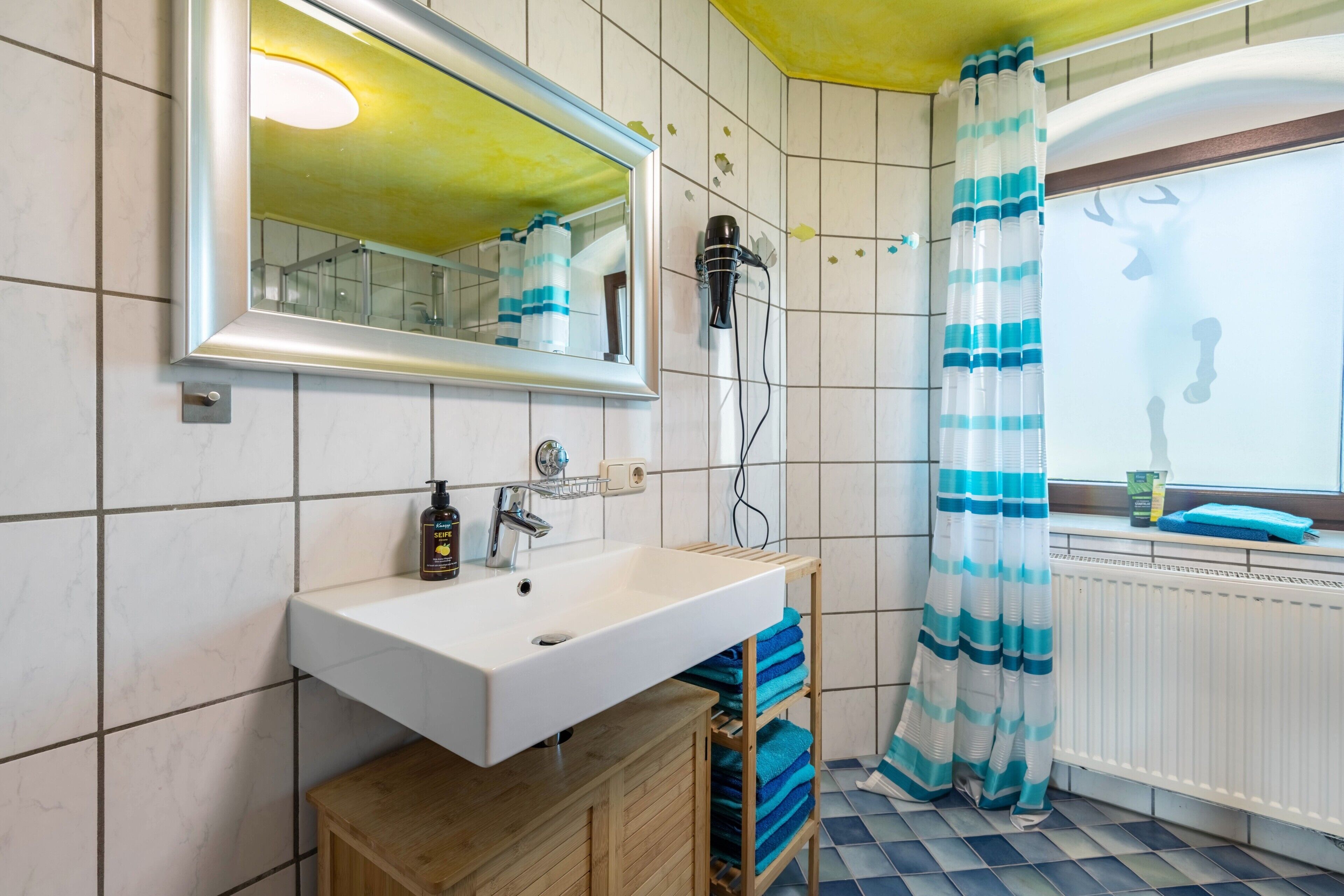 Ein Badezimmer mit weißem Waschbecken, einem Spiegel, einem Fön und einer Duschvorhang.