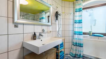 Ein Badezimmer mit weißem Waschbecken, einem Spiegel, einem Fön und einer Duschvorhang.