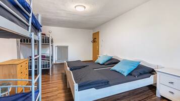 Ein Schlafsaalzimmer mit Etagenbetten, einem Schreibtisch, einem Stuhl, einem Heizkörper und einem Kleiderschrank.
