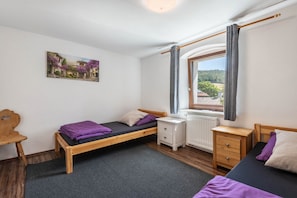 Un dormitorio con una cama individual, una silla de madera, una mesita de noche pequeña, un radiador y una ventana con cortinas.