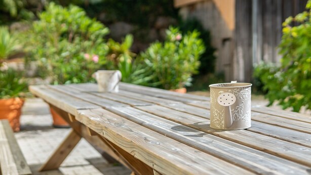 A wooden picnic table with a ceramic mug and a small white pot on it.