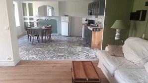 Uma sala de estar com um baú de madeira, um sofá branco e uma área de jantar com mesa e cadeiras.