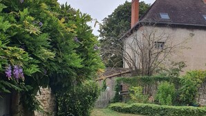 Uma área residencial com muro de pedra, gramado e uma casa com telhado e chaminé.