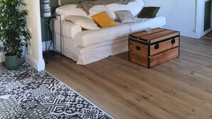 Uma sala de estar com sofá branco, um baú de madeira, tapete estampado e parede verde.