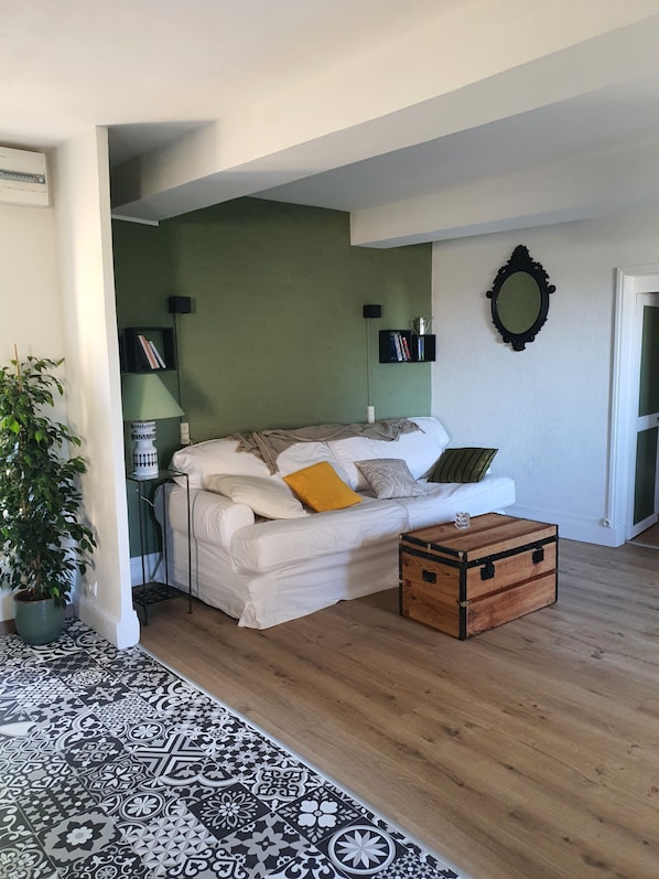 A living room with a white sofa, a wooden chest, a patterned rug, and a green wall.