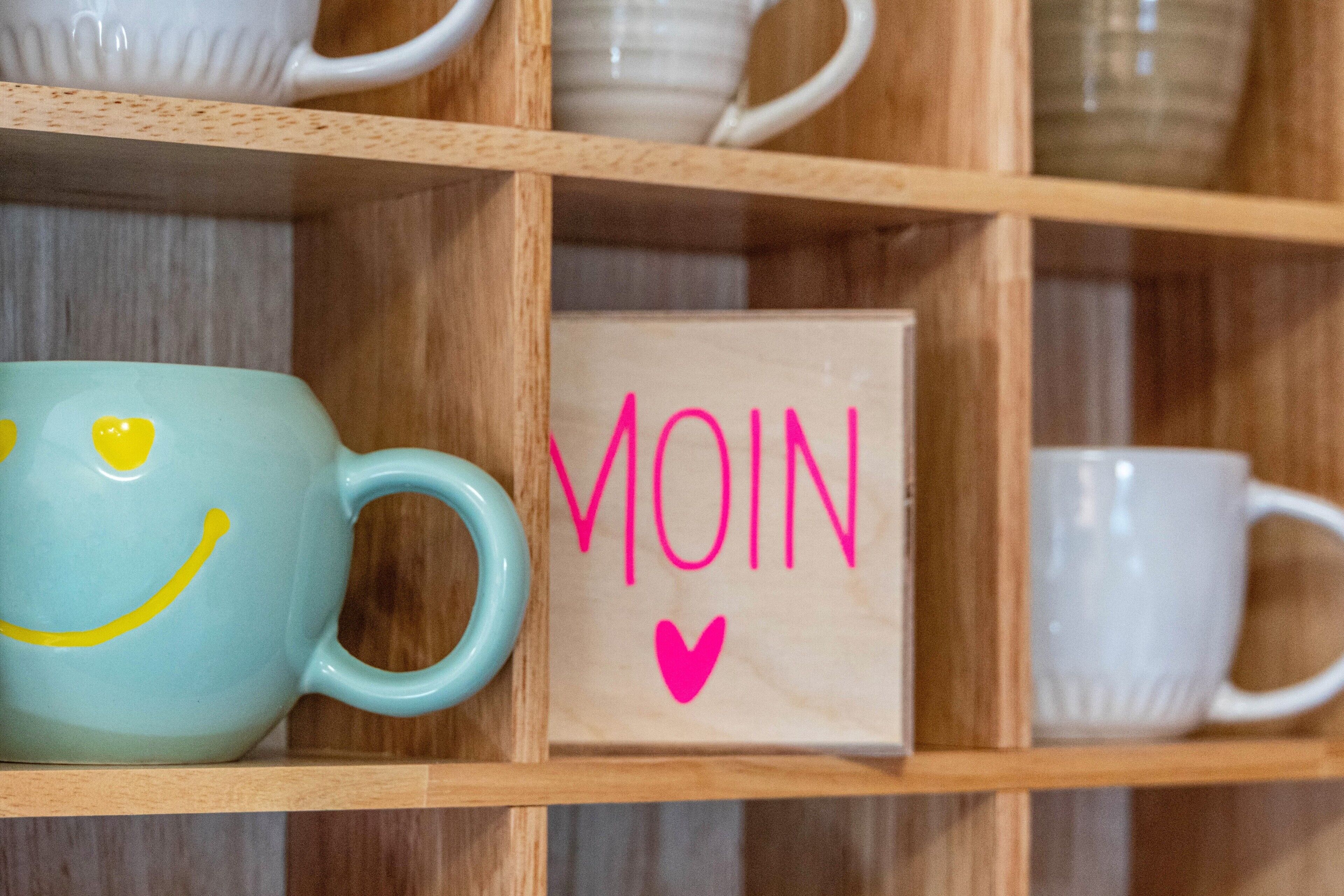 A shelf with ceramic mugs and a wooden box with the word 'MOIN' and a heart symbol.