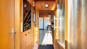 A wooden interior hallway with a door, a clock, and a view into a dining area. - Holiday Home Alma – Private Terrace, Wi-Fi, Garden & Coffee Delight Included (Wittmund)