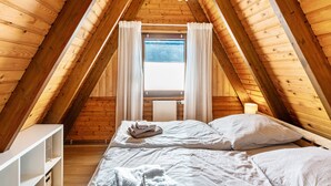 An attic bedroom with wooden beams, a window with curtains, a bed with pillows, and a bedside table. - Holiday Home Alma – Private Terrace, Wi-Fi, Garden & Coffee Delight Included (Wittmund)
