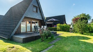 A modern house with a sloped roof, a deck, and a garden. - Holiday Home Alma – Private Terrace, Wi-Fi, Garden & Coffee Delight Included (Wittmund)