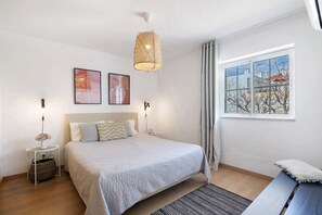 Ein Schlafzimmer mit einem großen Bett, Nachttischen, einer Pendelleuchte, einem Fenster mit Blick und einem an der Wand hängenden Kunstwerk.