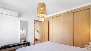 Een slaapkamer met een bed, een houten garderobe, een hanglamp en een bankje.