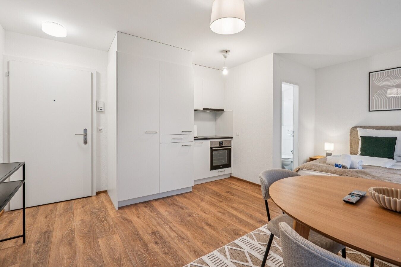 Une chambre d’hôtel compacte comprenant un coin cuisine, un espace repas et un lit avec une tête de lit.