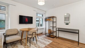 A modern living room with a TV, a round table, two chairs, a bookshelf, and a mirror. - Exclusive studio near city center - Color 4 (Zürich)