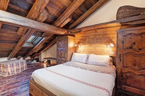 A wooden bedroom with a sloped ceiling, a bed with patterned bedding, and a small table with a checkered tablecloth. - '5 Coppafen' Apartment for Families with Balcony (Plan-d'Introd)