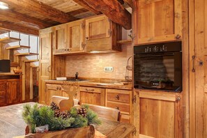 A rustic kitchen with wooden cabinets, a Bosch oven, and a dining table with pine decorations. - '5 Coppafen' Apartment for Families with Balcony (Plan-d'Introd)