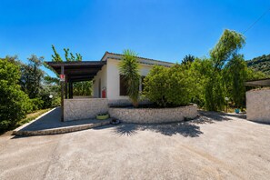 Ein Haus mit überdachter Veranda, einer Steinmauer und einem Garten mit einer Palme.