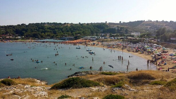 Une plage avec des bateaux, des parasols et des gens.