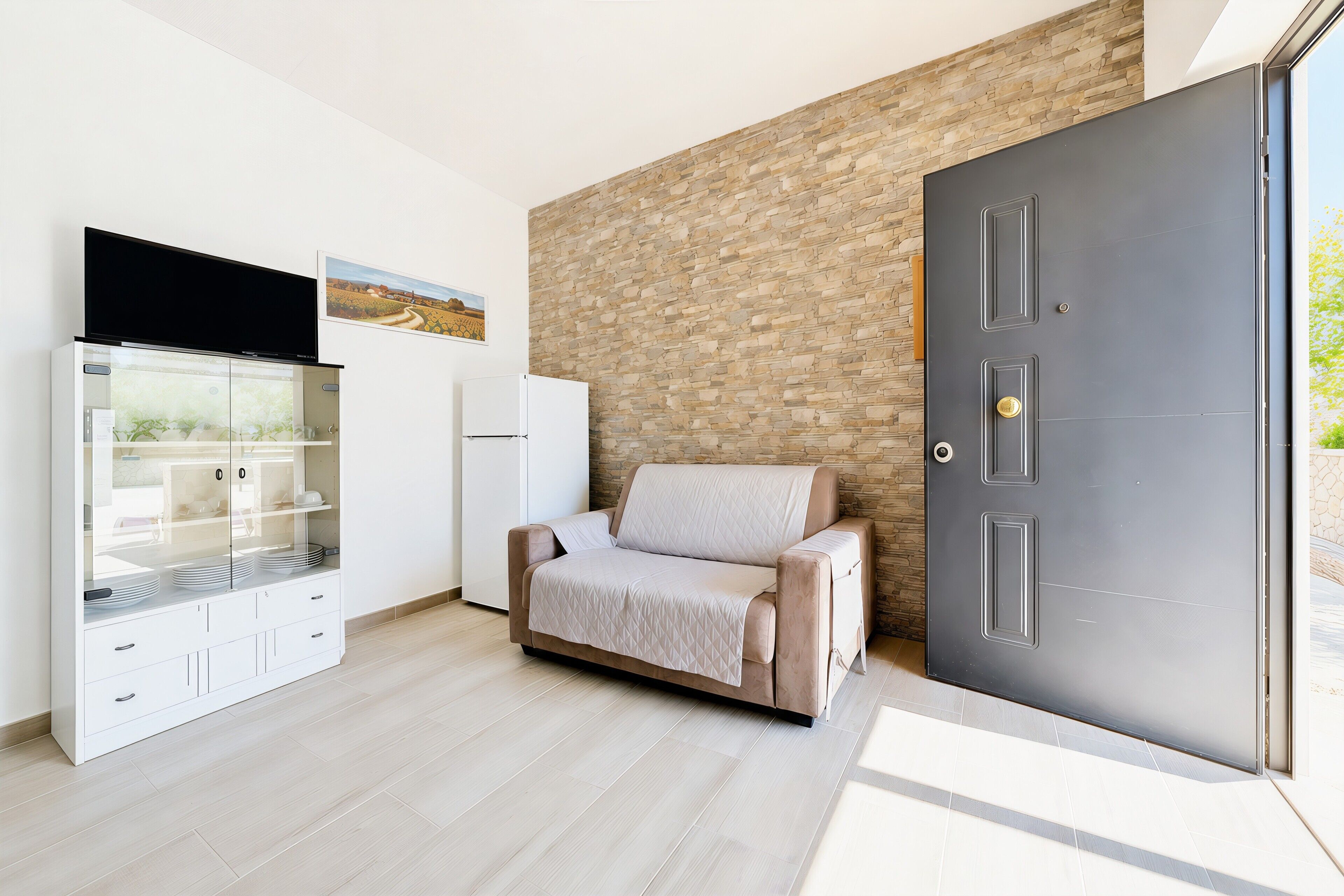 Una habitación moderna con un sofá, un aparador con puertas de vidrio, un televisor de pantalla plana y una puerta con una pared texturizada detrás.