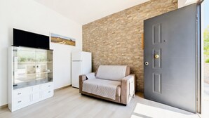 Une pièce moderne comprenant un canapé, un meuble avec des portes en verre, un téléviseur à écran plat et une porte devant laquelle se trouve un mur à texture.