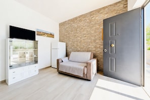 Quarto moderno com sofá, armário de vidro, televisão de tela plana e porta com parede texturizada ao fundo.