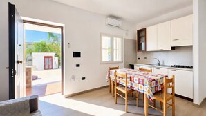 Une cuisine moderne avec une table à manger, des chaises et une porte ouverte donnant sur l’extérieur.