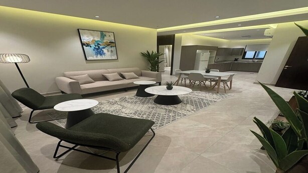 Una sala moderna con un sofá, dos sillones, una mesa de centro y un comedor con una mesa y sillas.