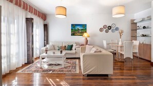Un salon moderne avec un canapé, une table basse et une table à manger. On y trouve un tableau au mur, une lampe et une bibliothèque.