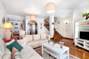 Een woonkamer met een bank, salontafel en tv-meubel. Er is een trap die naar een hoger niveau leidt.