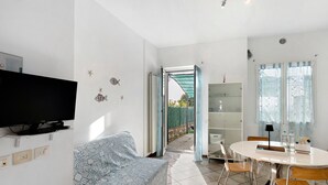 Una sala de estar con un sofá, un televisor, una mesa de comedor con sillas y una estantería.
