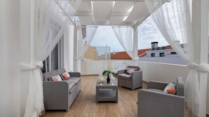 Un balcon agrémenté de meubles en osier, de rideaux blancs et offrant une vue sur les immebles.