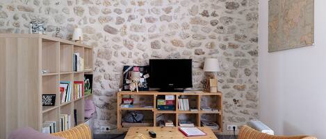 Una sala de estar con pared de piedra, una estantería de madera, un televisor y sillones de mimbre.