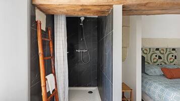 Een badkamer met een douche, een houten ladder, een klein krukje en een bed met decoratieve beddengoed.