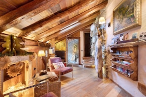 Ein rustikales Interieur mit Holzbalken, einem Kamin, einem bequemen Ohrensessel und einem Bücherregal.