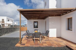 A patio with a table and chairs, a pergola, and a view of a white building.