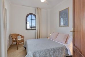 A bedroom with a bed, a chair, a window, and a painting on the wall.