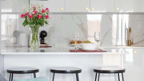 Eine moderne Küche mit einer weißen Marmorarbeitsplatte, drei schwarzen Barhocker und einer Vase mit rosa Blumen.