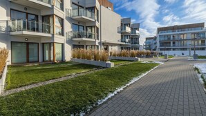 Ein modernes, mehrstöckiges Wohngebäude mit Balkonen, einem gepflasterten Weg und einer bepflanzten Grünfläche mit Gras und Sträuchern.