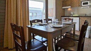 Un comedor con una mesa y sillas de madera, una ventana con cortinas, y una cocina al fondo.
