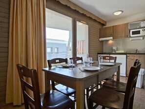 Un comedor con una mesa y sillas de madera, una ventana con cortinas, y una cocina al fondo.