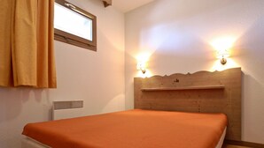 Una cama individual con colcha naranja en una habitación con cabecera de madera y dos lámparas de pared.