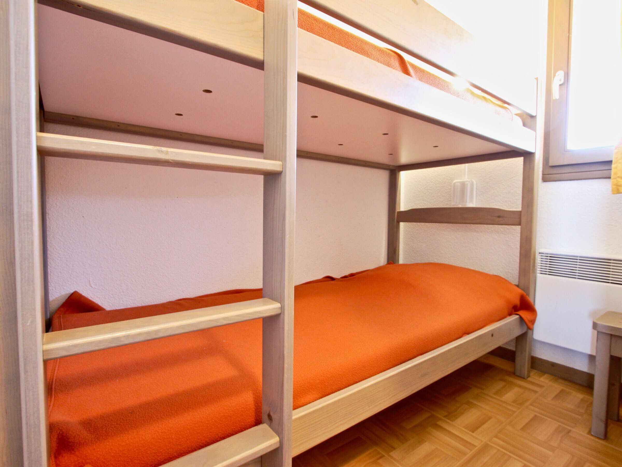 Une chambre avec un lit superposé, dont les structures sont en bois et la literie est orange.