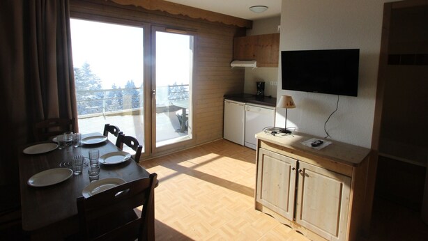 Cocina compacta con comedor, puerta corrediza de vidrio a un balcón y un televisor montado.