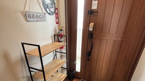 Una puerta de madera con buzón, extintor, cartel de bienvenida y zapatero con pantuflas.